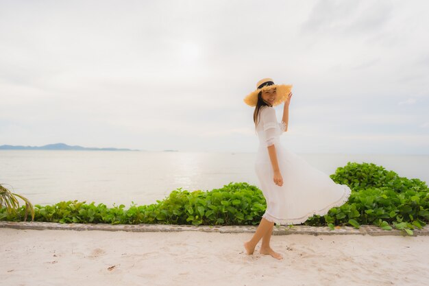 Sombrero asiático hermoso del desgaste de mujer del retrato con ocio feliz de la sonrisa en la playa y el mar en vacaciones del día de fiesta