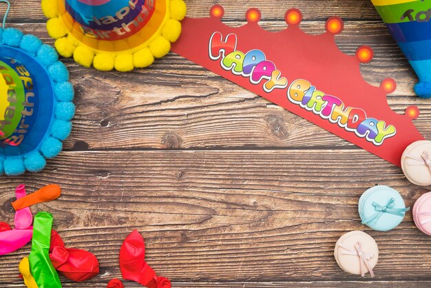 Sombrero de cumpleaños; corona; globos y macarons en el fondo de madera