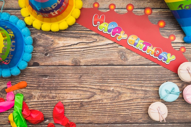 Sombrero de cumpleaños; corona; globos y macarons en el fondo de madera