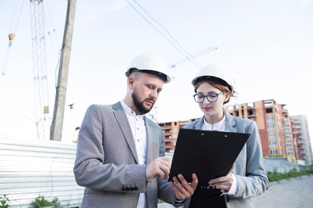 Sombrero duro que lleva del arquitecto de sexo femenino y de sexo masculino joven que mira el tablero