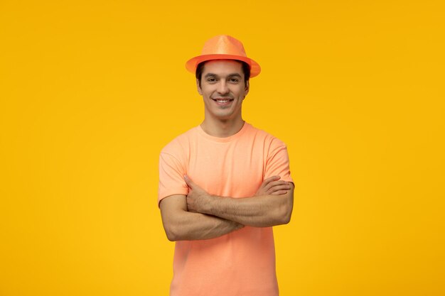 Sombrero naranja chico lindo joven sonriendo con las manos cruzadas en camiseta naranja