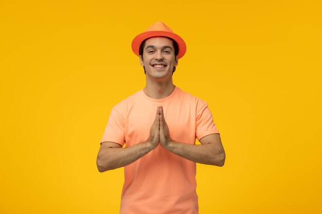 Sombrero naranja lindo chico joven en camisa naranja con el sombrero rezando y sonriendo