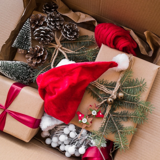 Sombrero de Navidad cerca de cajas de regalo, ramas de abeto decoradas en caja de cartón