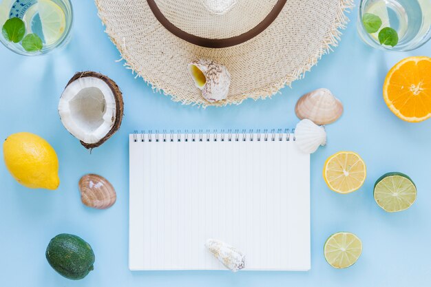 Sombrero de paja con frutas exóticas y cuaderno.