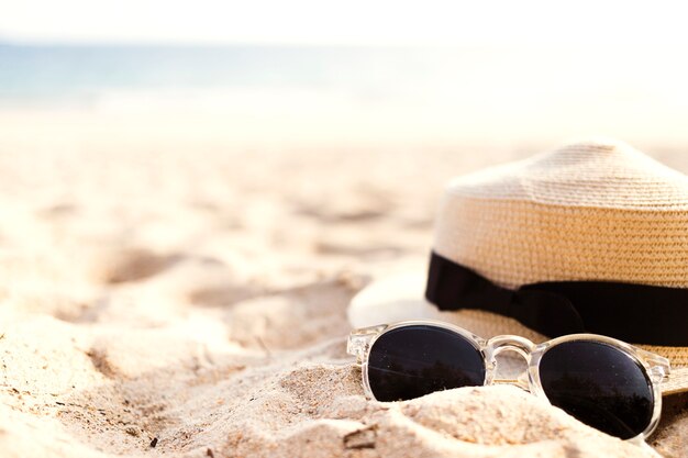 Sombrero de paja y gafas de sol en la arena cerca de la costa
