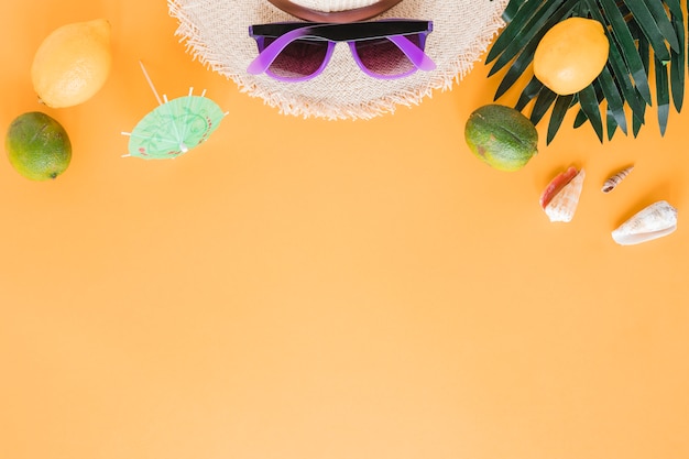 Sombrero de paja con gafas de sol, conchas y frutas.