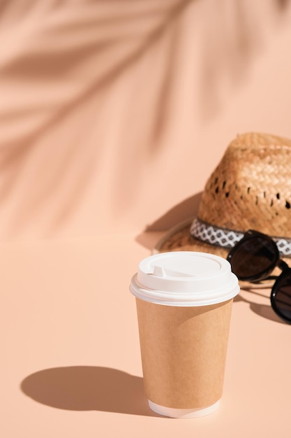 Sombrero de paja de taza de café y gafas de sol sobre un fondo beige claro sombreado por marco vertical de hojas de palma Soñando con el verano y la diversión disfrutando de la vida vacaciones viajes concepto de turismo