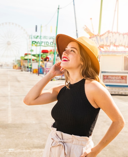 Sombrero que lleva sonriente de la mujer joven que se coloca en el parque de atracciones