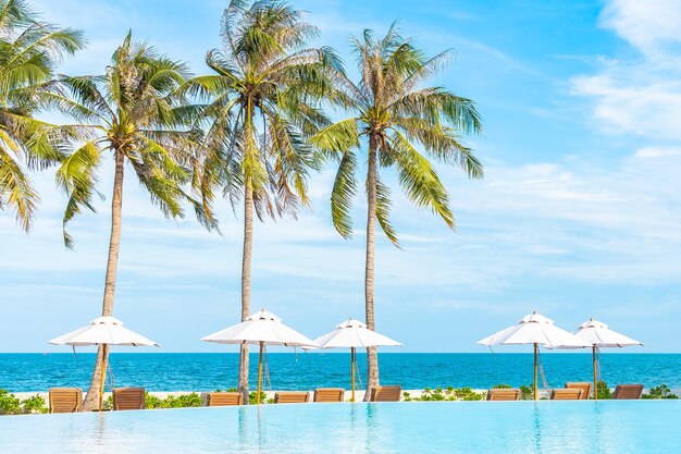 Sombrilla y tumbona alrededor de la piscina al aire libre en el hotel resort con mar océano playa y palmera de coco