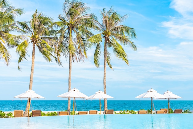 Sombrilla y tumbona alrededor de la piscina al aire libre en el hotel resort con mar océano playa y palmera de coco