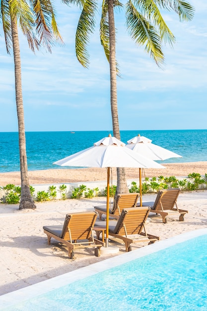 Foto gratuita sombrilla y tumbona alrededor de la piscina al aire libre en el hotel resort con mar océano playa y palmera de coco