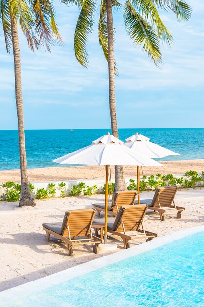 Sombrilla y tumbona alrededor de la piscina al aire libre en el hotel resort con mar océano playa y palmera de coco