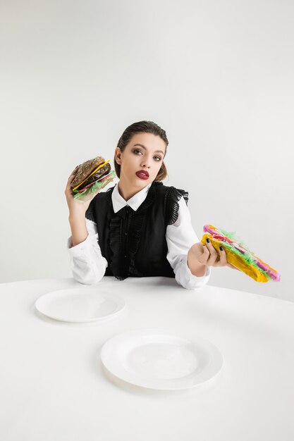 Somos lo que comemos. Mujer come hamburguesa y hot-dog de plástico, concepto ecológico