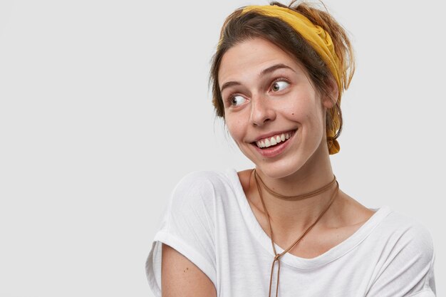 Soñadora complacida joven mujer caucásica con amplia sonrisa, apariencia agradable, piel sana, usa diadema