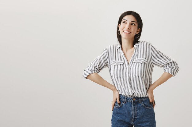 Soñadora complacida joven sonriendo como idea interesante, mirando en la esquina superior izquierda