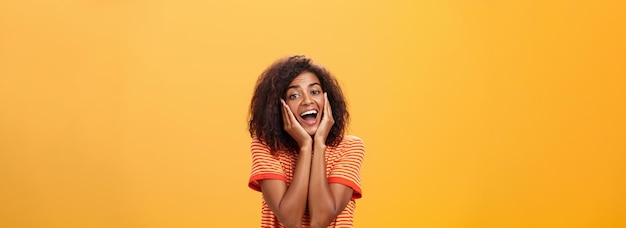 Foto gratuita soñadora, guapa, elegante, joven mujer africana con el peinado rizado, suspirando, inclinando la cabeza sobre las palmas de las manos.