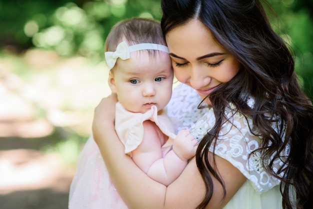 Soñadora joven mamá sostiene a su pequeña hija posando fuera