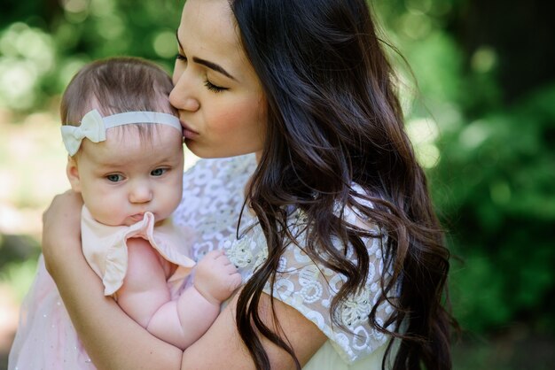 Soñadora joven mamá sostiene a su pequeña hija posando fuera