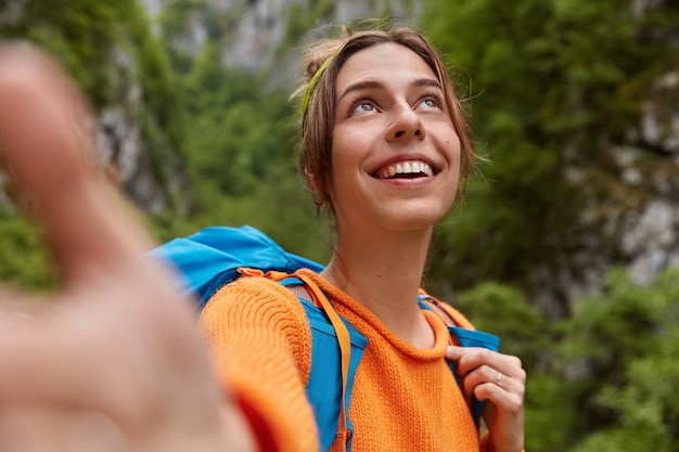 Soñadora joven positiva enfocada hacia arriba, hace retrato selfie