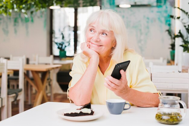 Soñadora sonriente anciana con smartphone