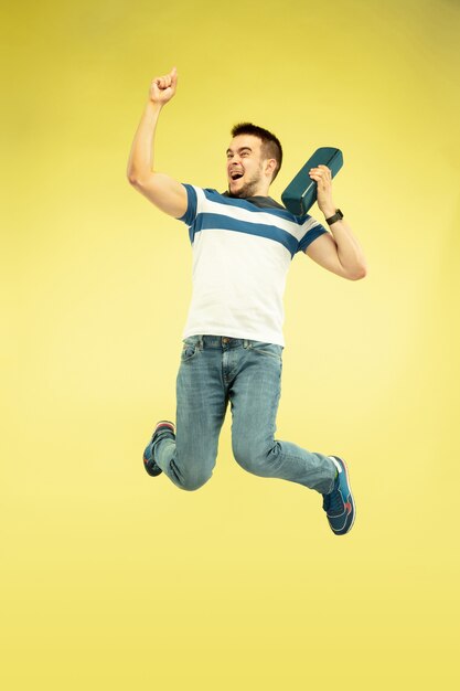 Sonido del cielo. Retrato de cuerpo entero de hombre feliz saltando con gadgets sobre fondo amarillo