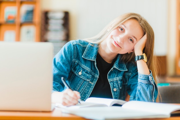 Sonriendo adolescente haciendo notas cerca de la computadora portátil