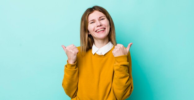 Sonriendo alegremente y luciendo feliz sintiéndose despreocupado y positivo con ambos pulgares hacia arriba