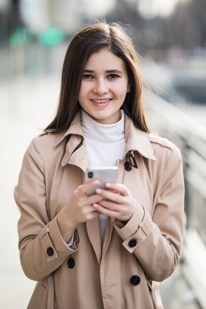 Sonriendo bastante joven modelo envía un mensaje de texto a su teléfono afuera