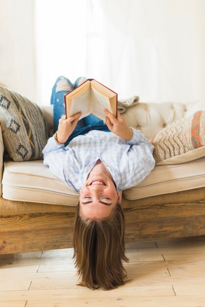 Sonriendo boca abajo mujer sosteniendo libro de tapa dura