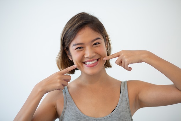 Sonriendo bonita mujer asiática apuntando a sus dientes