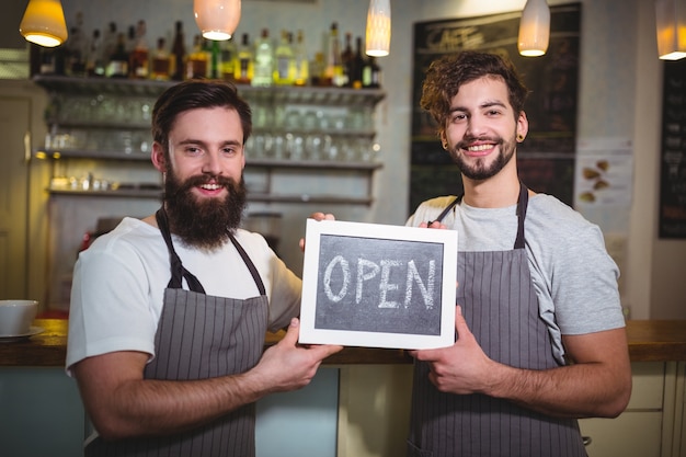 Sonriendo camarero coloca con la tarjeta muestra abierta en el café