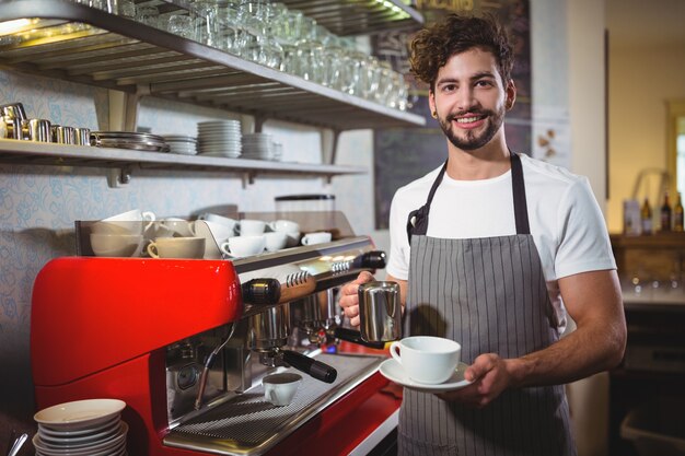 Sonriendo camarero toma una taza de café en el contador en el café