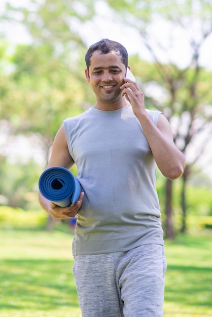 Sonriendo chico indio hablando por teléfono en su camino a la clase de yoga.