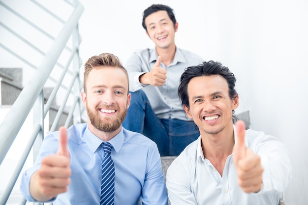 Sonriendo colegas mostrando pulgares en las escaleras