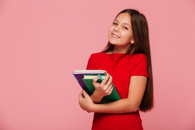 Sonriendo colegiala sosteniendo libros y mirando