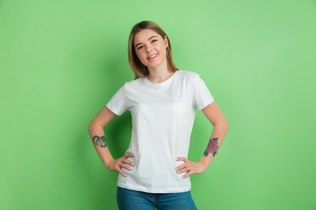 Sonriendo, confiado. Retrato de mujer joven caucásica en la pared verde del estudio