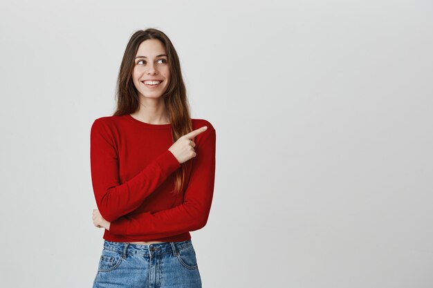 Sonriendo contenta, atractiva mujer apuntando y mirando la esquina superior derecha