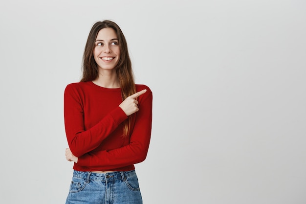 Sonriendo contenta, atractiva mujer apuntando y mirando la esquina superior derecha