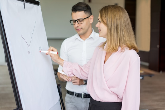 Foto gratuita sonriendo dibujo diagrama de empresaria a colega masculino.