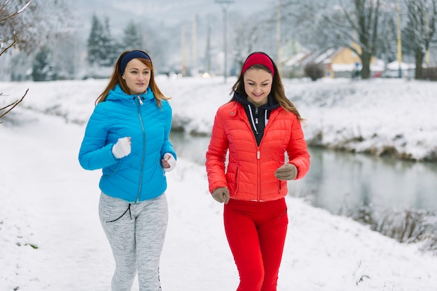 Sonriendo dos amigas corriendo en la temporada de invierno