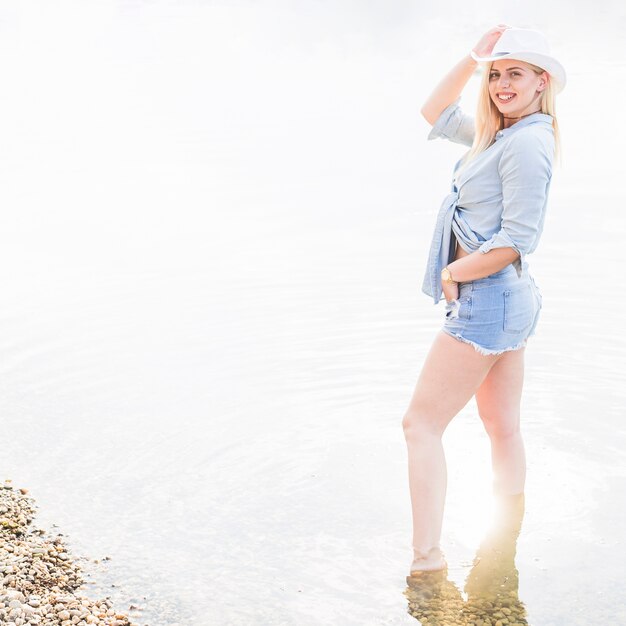 Sonriendo a la elegante mujer joven de pie en el lago