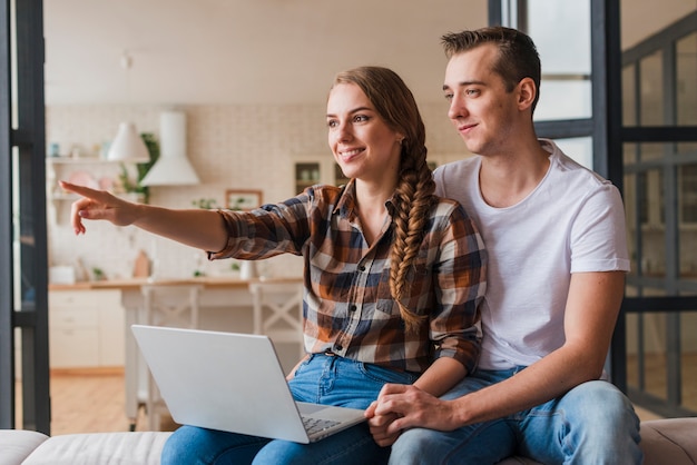 Sonriendo encantadora pareja con la computadora mirando a otro lado