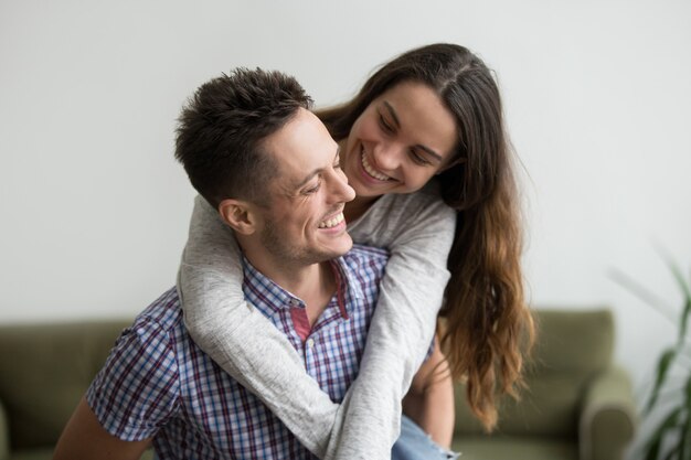 Sonriendo esposa riendo abrazando joven marido a cuestas en su casa