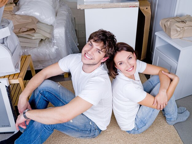 Sonriendo feliz pareja joven sentada espalda con espalda después de moverse - ángulo alto