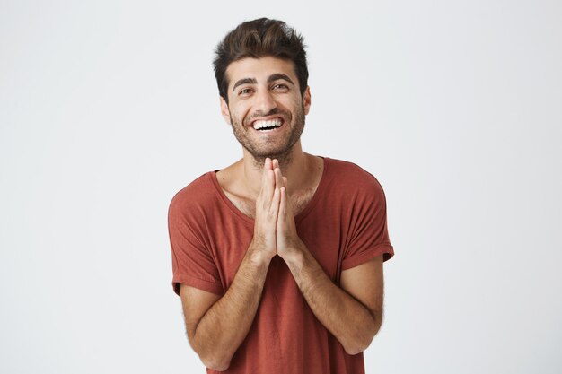 Sonriendo guapo italiano sin afeitar chico sosteniendo las palmas presionadas juntas delante de él sintiéndose feliz por el regalo de cumpleaños de la esposa.