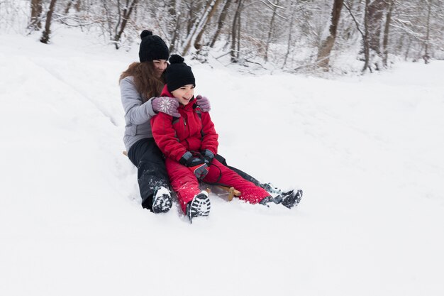Sonriendo hermano y hermana disfrutando de trineo juntos en invierno