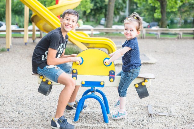 Sonriendo hermano y hermana jugando balancín en el patio de recreo