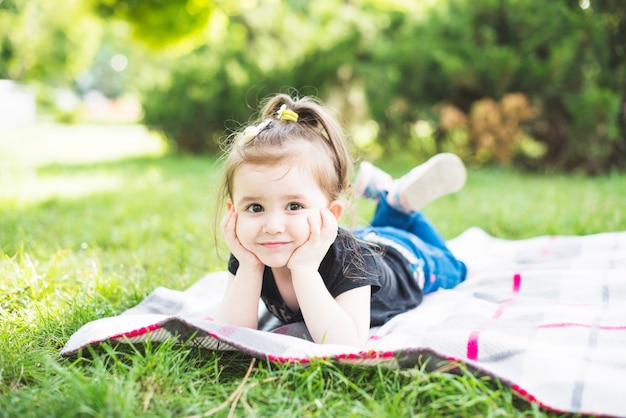 Sonriendo a hermosa niña acostada sobre una manta sobre la verde hierba