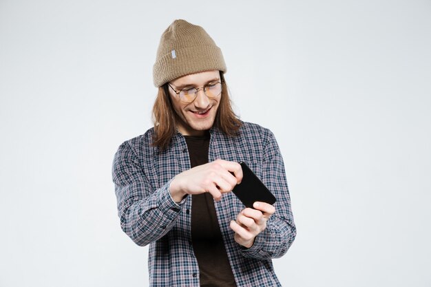 Sonriendo hipster en anteojos jugando en smartphone