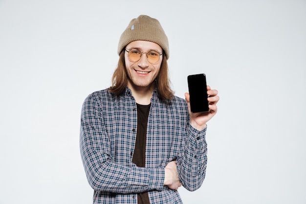 Sonriendo hipster en anteojos mostrando la pantalla del teléfono inteligente en blanco